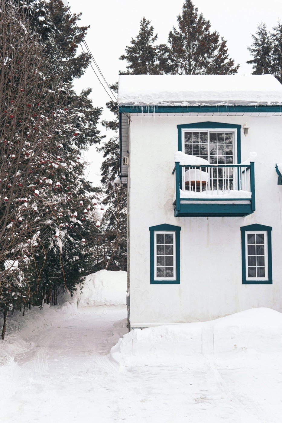Maison québécoise blanche aux encadrements bleu profond, avec balcon, sous la neige.